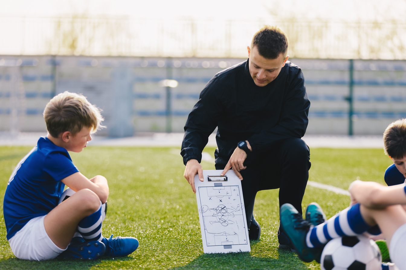 Entrenador proporcionando instrucciones tácticas de fútbol a niños con entusiasmo.