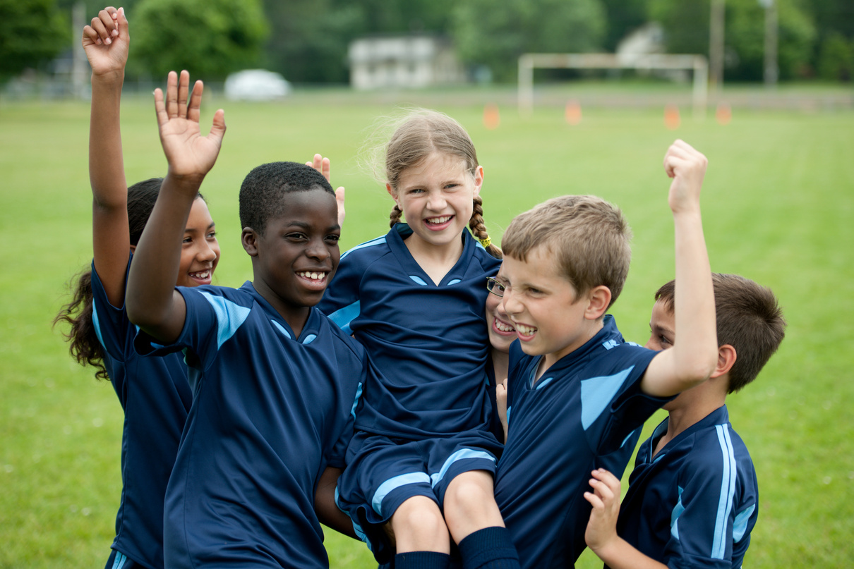 Niños felices y celebrando con abrazos en el campo de entrenamiento de fútbol.